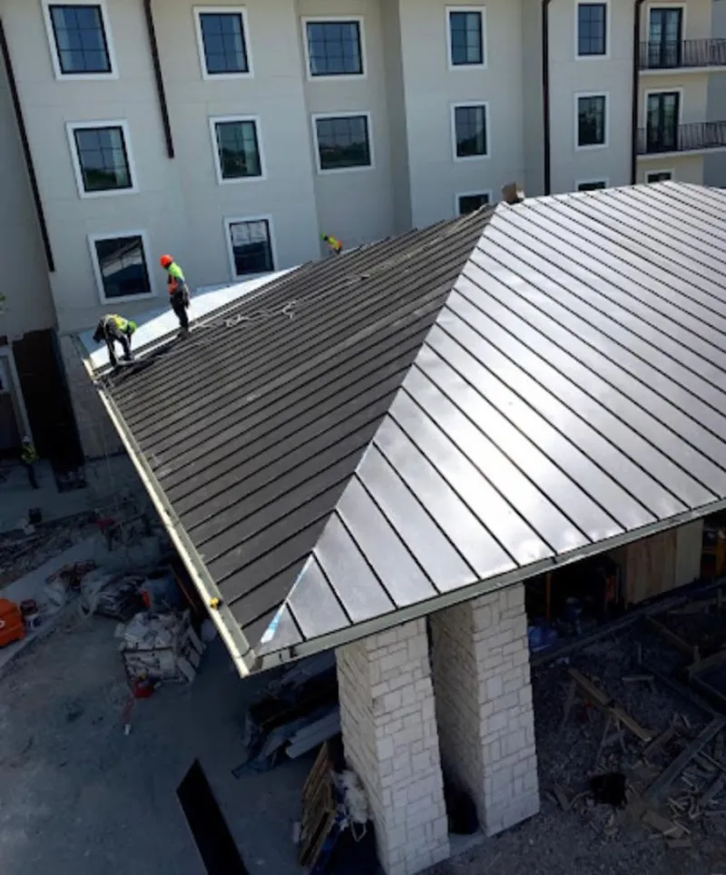 Crew installing standing seam metal roof panels on a commercial project in Newton